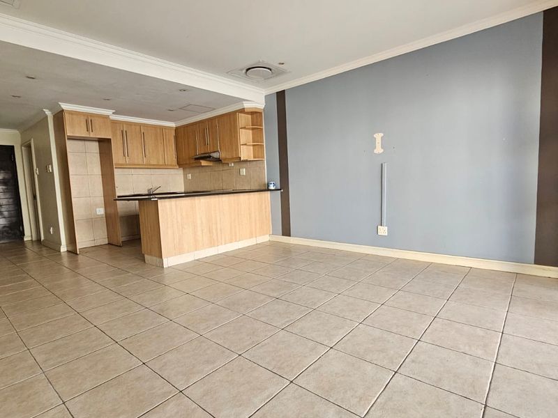 Spacious open-plan living and kitchen area featuring tiled flooring, built-in wooden cabinetry, and a breakfast bar, offering a versatile layout for modern living.