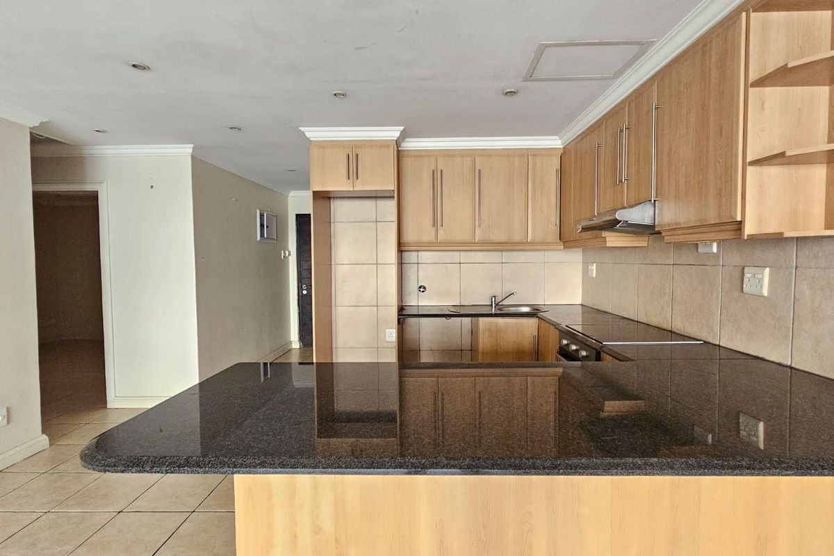 A functional kitchen featuring granite countertops, ample wooden cabinetry, a tiled backsplash, and a breakfast bar, presented in a clean, empty space.