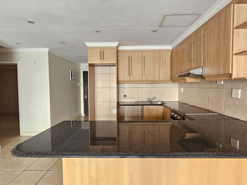 A functional kitchen featuring granite countertops, ample wooden cabinetry, a tiled backsplash, and a breakfast bar, presented in a clean, empty space.