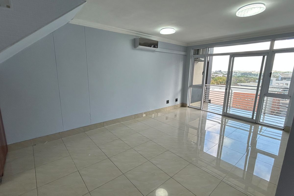An empty living room featuring tiled flooring, an air conditioning unit, and large sliding glass doors leading to a balcony with an urban view.
