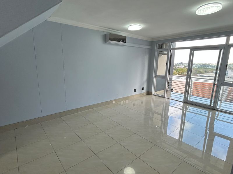 An empty living room featuring tiled flooring, an air conditioning unit, and large sliding glass doors leading to a balcony with an urban view.