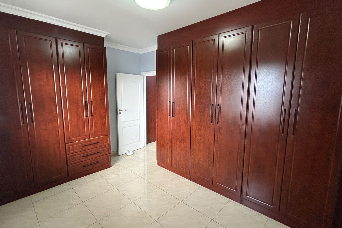 A spacious bedroom featuring extensive dark wood built-in cabinetry, neutral tiled flooring, and classic coving detail.