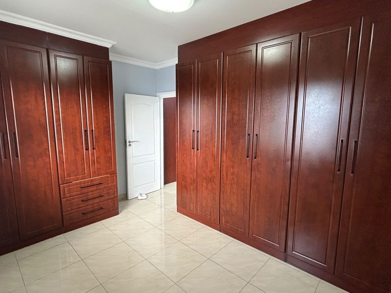 A spacious bedroom featuring extensive dark wood built-in cabinetry, neutral tiled flooring, and classic coving detail.