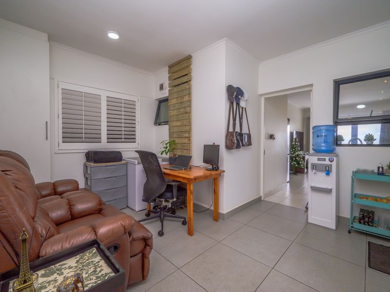 A functional home office space featuring tiled flooring, built-in storage, plantation shutters, and recessed lighting, offering a versatile area for work or study.