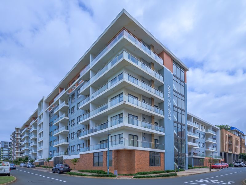 Modern multi-story apartment building featuring glass-fronted balconies, brick detailing, and a prominent corner facade with large windows.