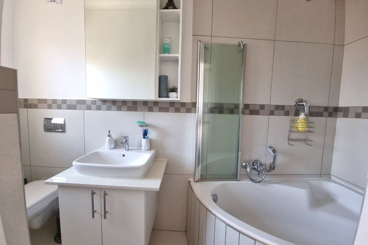 Modern bathroom featuring a corner bathtub with a glass screen, a vessel sink vanity, and a wall-mounted toilet with neutral wall tiling.