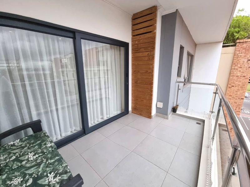 A modern apartment balcony featuring tiled flooring, a glass balustrade with stainless steel railings, and decorative timber slat wall cladding.