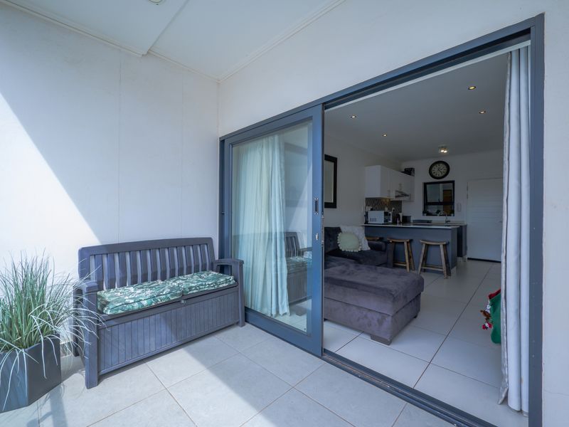 A covered balcony with tiled flooring, featuring a large sliding glass door that opens into an open-plan living and kitchen area.