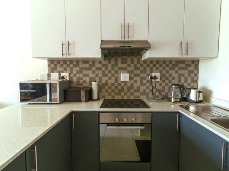 Modern kitchen featuring two-tone cabinetry, stone countertops, mosaic tile backsplash, and integrated stainless steel appliances including an oven and hob.