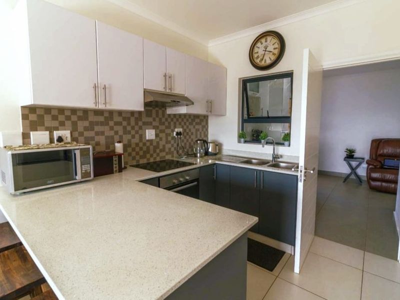 Modern kitchen featuring quartz countertops, built-in oven, electric hob, extractor fan, and ample cabinetry with a tiled backsplash.