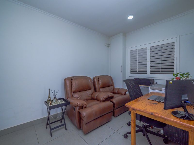 A functional home office space featuring tiled flooring, plantation shutters, and neutral wall finishes, suitable for a dedicated workspace or study area.