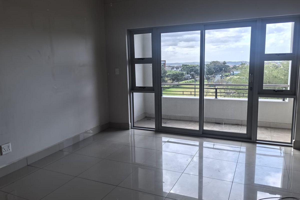 An empty, sunlit living area featuring polished tile flooring and large sliding glass doors that open onto a private balcony with scenic views.