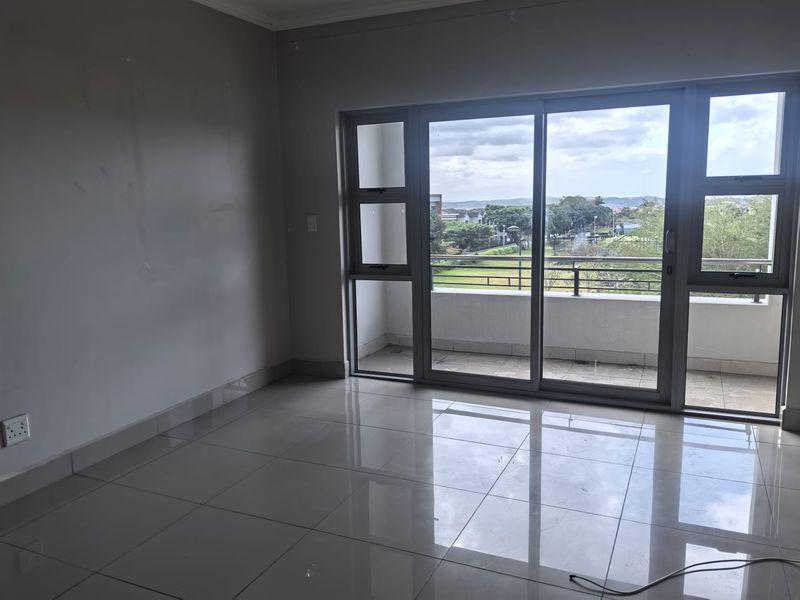 An empty, sunlit living area featuring polished tile flooring and large sliding glass doors that open onto a private balcony with scenic views.
