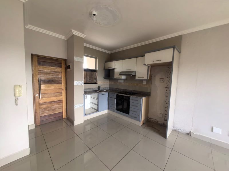A compact kitchen featuring built-in cabinetry, granite countertops, and integrated appliances, currently vacant and requiring minor cosmetic repairs to the cabinetry and wall finishes.