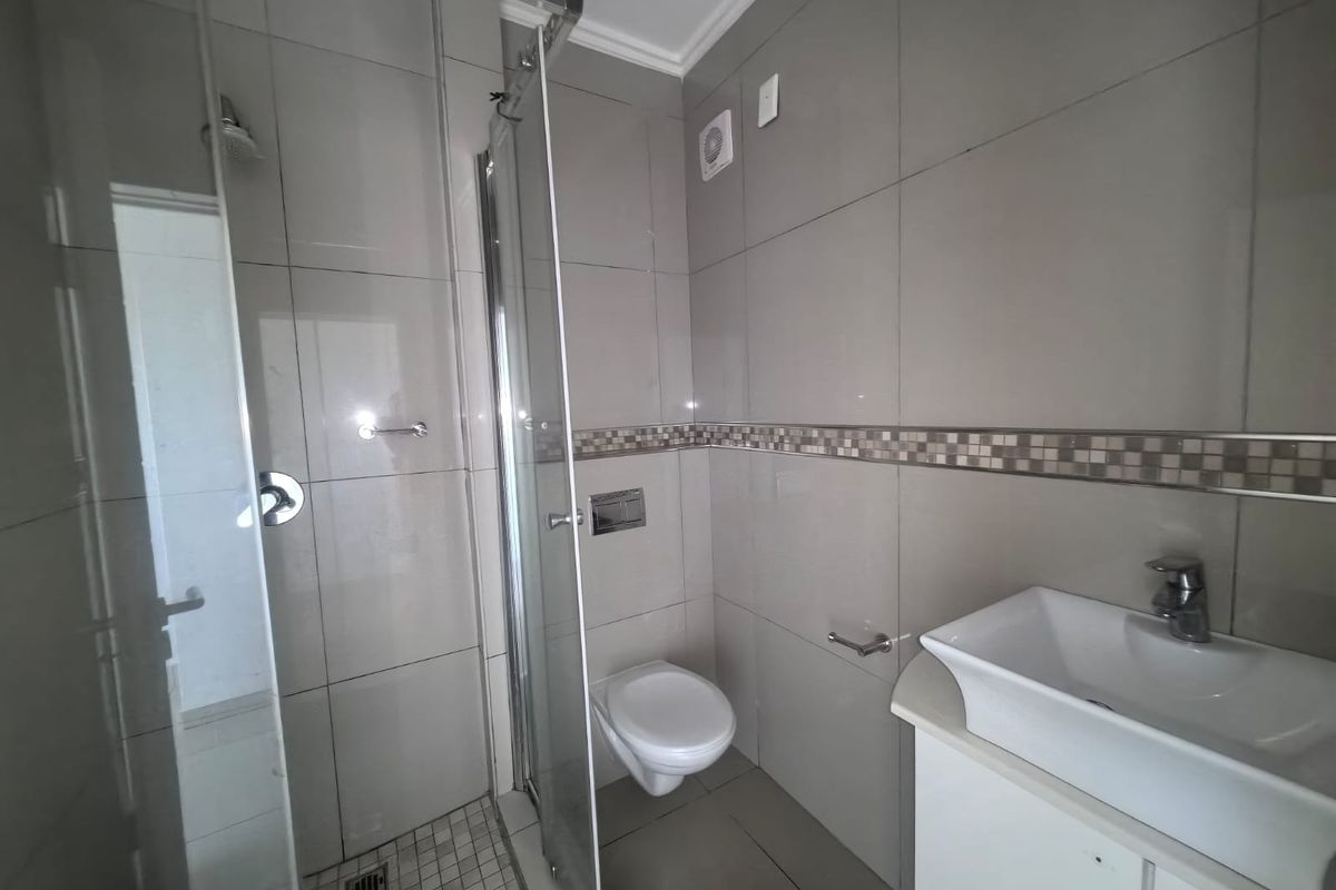 Modern bathroom featuring a glass shower enclosure, wall-mounted toilet, and a vanity basin with neutral wall and floor tiling.