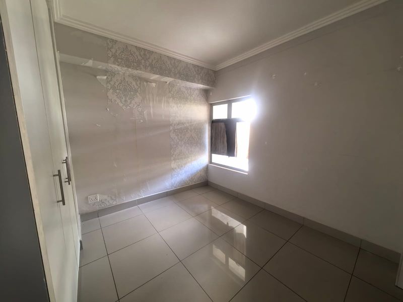 An empty bedroom featuring tiled flooring, a built-in wardrobe, and damaged wallpaper requiring repair or replacement.