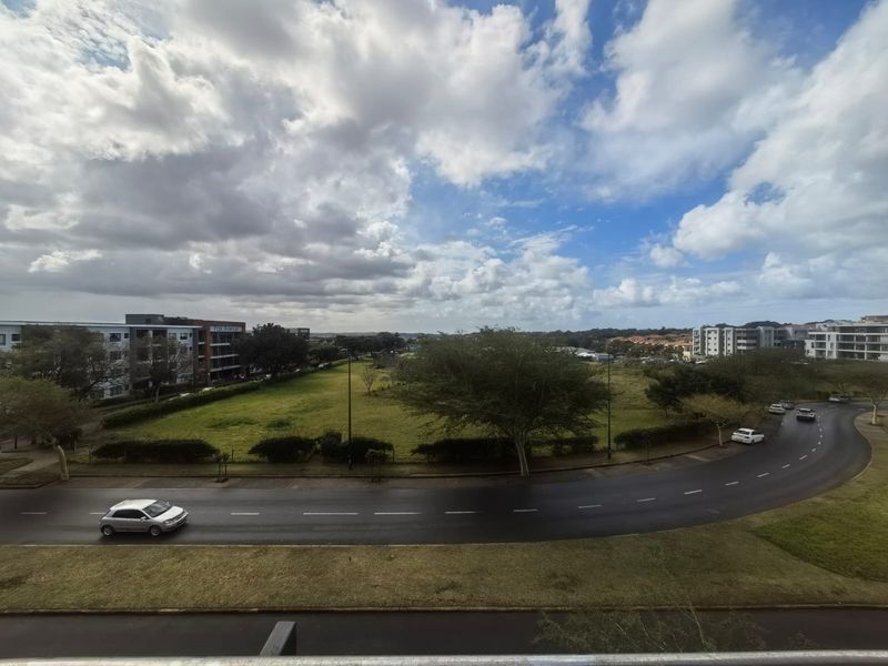 An elevated view overlooking a suburban street, green space, and surrounding apartment complexes under a cloudy sky.
