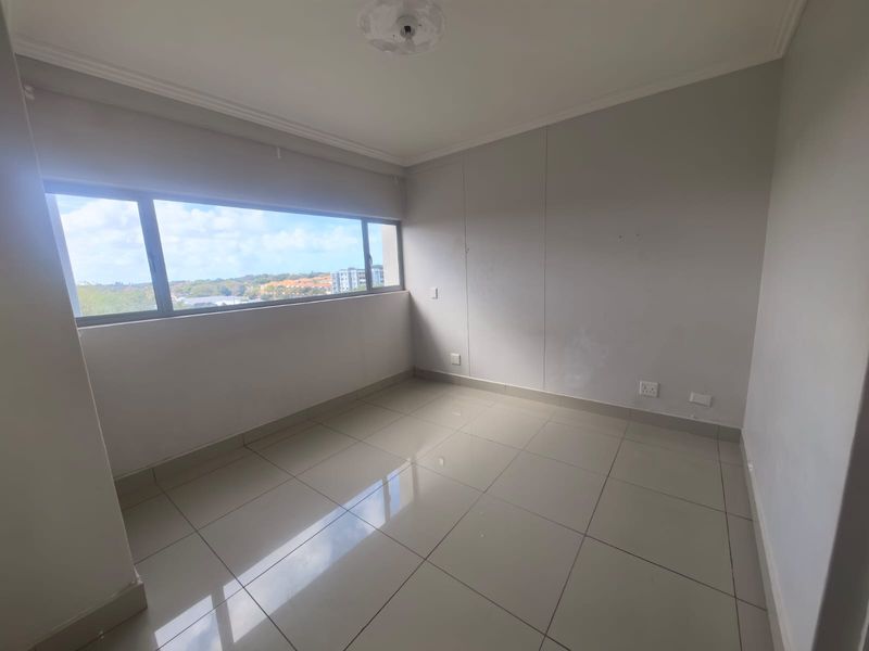 An empty bedroom featuring tiled flooring, neutral walls, and a large horizontal window providing natural light and an elevated view.