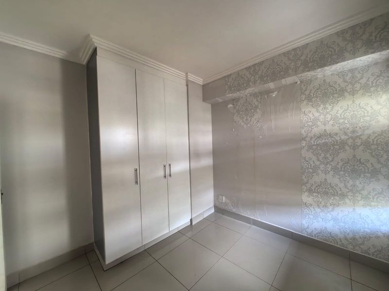 A bedroom featuring built-in cupboards, tiled flooring, and decorative crown molding, currently showing signs of wear on the wallpaper.