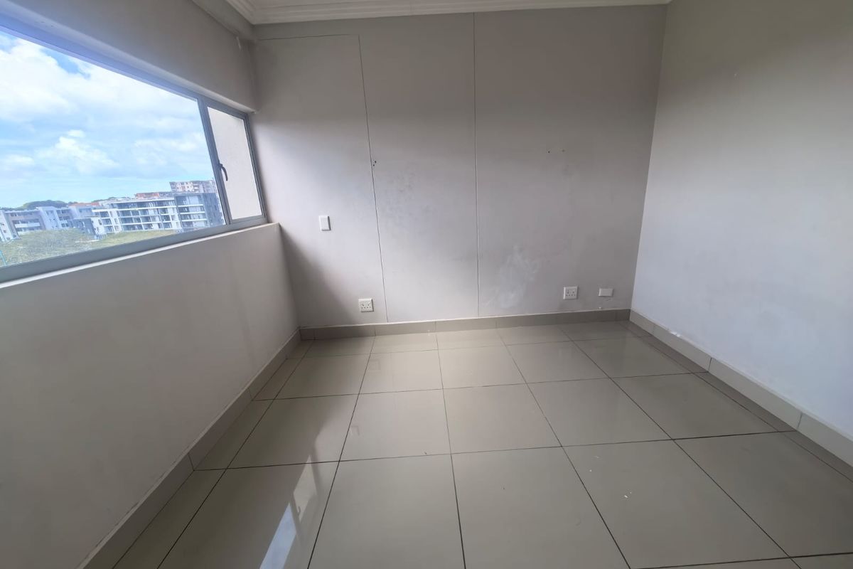 An empty bedroom featuring neutral tiled flooring, large sliding windows with an urban view, and standard electrical fixtures.