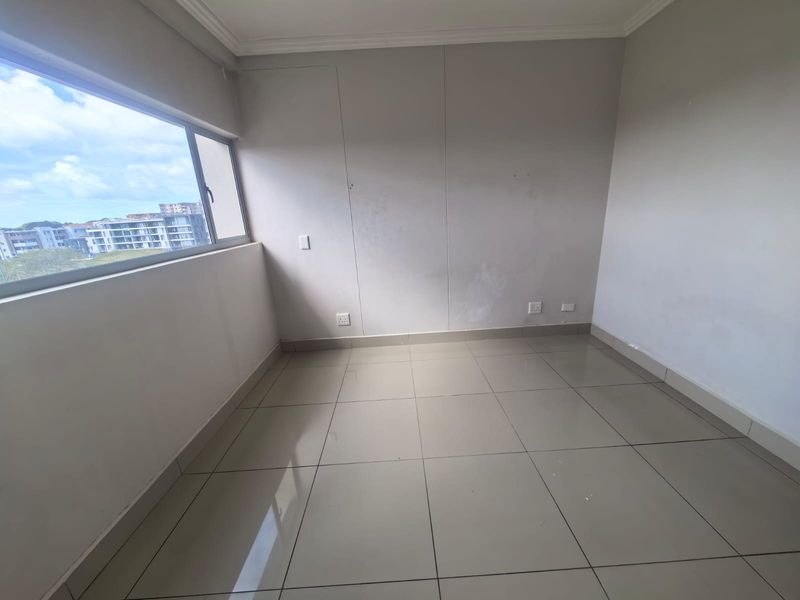 An empty bedroom featuring neutral tiled flooring, large sliding windows with an urban view, and standard electrical fixtures.