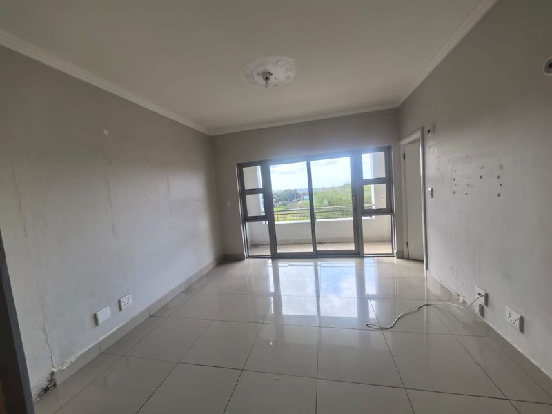 An empty living room featuring tiled flooring, coving, and a large sliding glass door leading to a balcony.