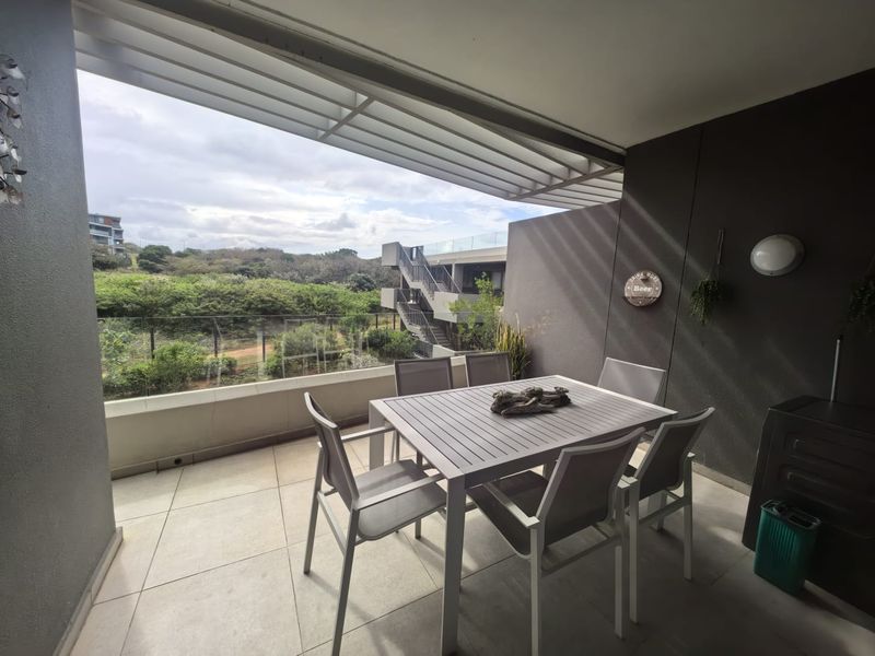 A covered balcony featuring tiled flooring, a glass balustrade, and a louvred roof, offering an open view of the surrounding landscape.