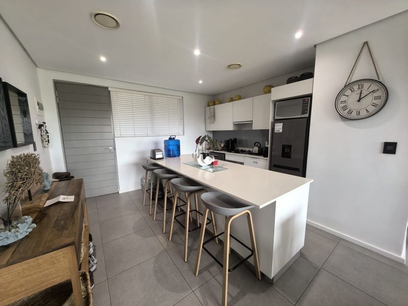 Modern kitchen featuring a central island with quartz countertops, built-in microwave, sleek cabinetry, and neutral tiled flooring in an open-plan layout.