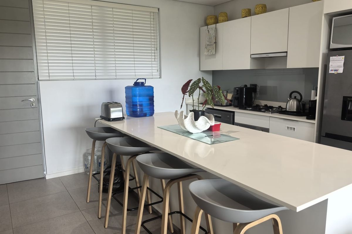 Modern kitchen featuring a large central island with quartz countertops, sleek cabinetry, integrated appliances, and neutral tiled flooring.