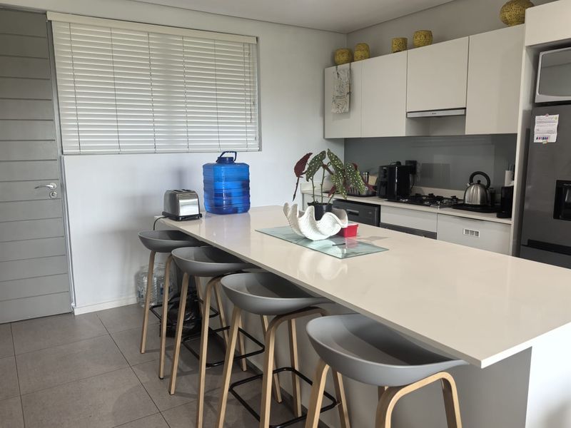 Modern kitchen featuring a large central island with quartz countertops, sleek cabinetry, integrated appliances, and neutral tiled flooring.