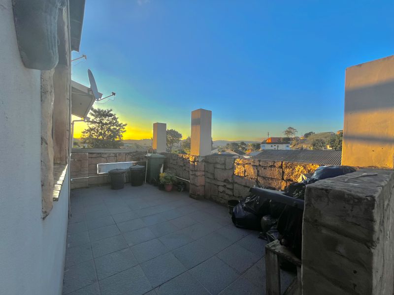 An open-air balcony featuring tiled flooring, stone-clad perimeter walls, and concrete structural pillars, offering an elevated view of the surrounding neighborhood.