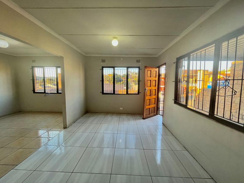 Spacious open-plan living area featuring neutral tiled flooring, security bars on windows, and direct access to the exterior.