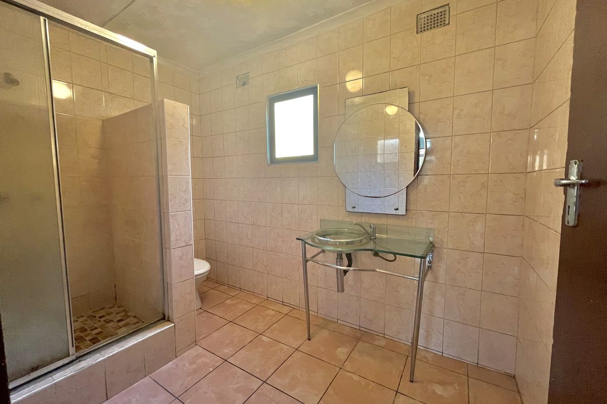 A functional bathroom featuring a glass shower enclosure, pedestal washbasin, and neutral ceramic tiling throughout.