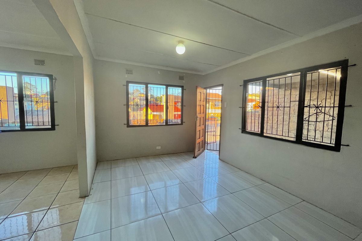 An empty, open-plan living area featuring tiled flooring, security bars on windows, and a timber entrance door, offering a blank canvas for interior design.