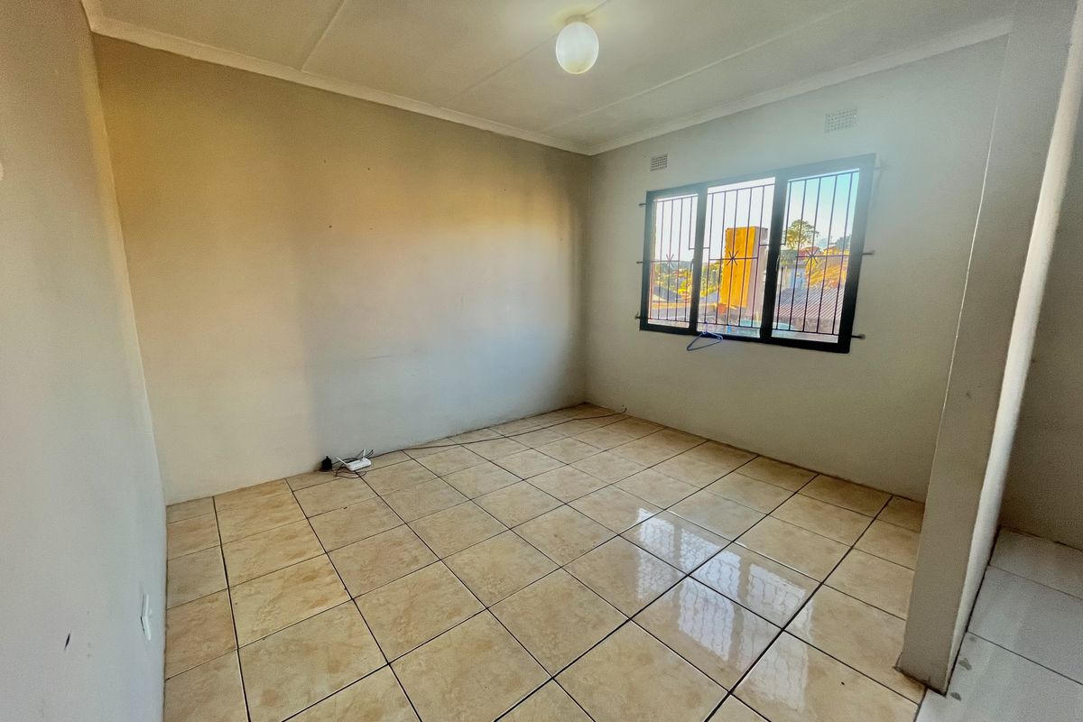 An empty bedroom featuring ceramic floor tiles, neutral walls, and a window fitted with security bars.