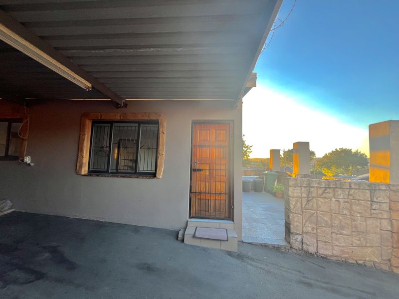 Exterior view of the property entrance featuring a covered driveway, timber door with security gate, and an adjacent tiled patio area.