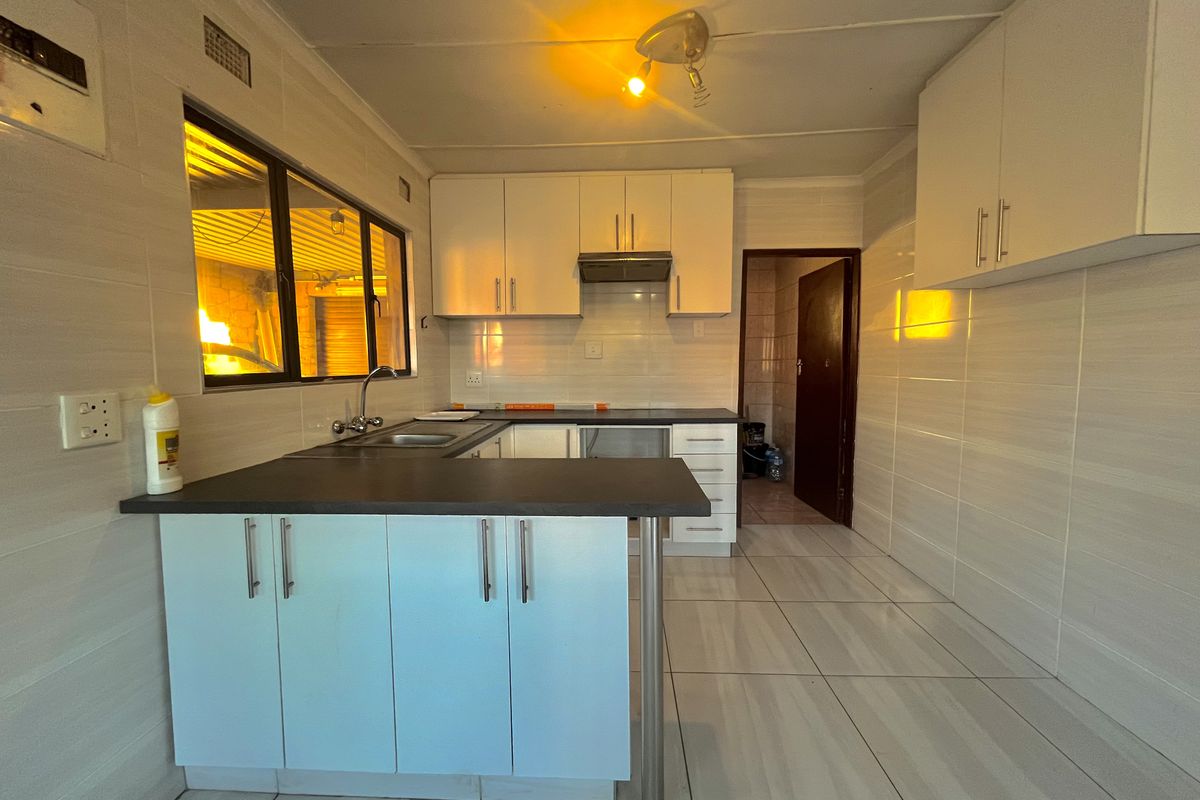 A functional kitchen featuring tiled walls and floors, built-in cabinetry, a stainless steel sink, and an extractor fan, ready for modern updates.