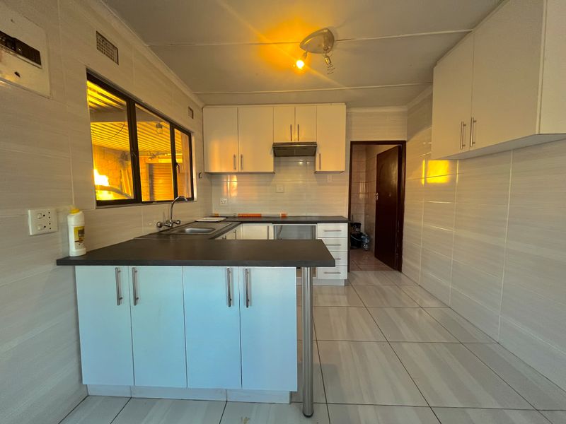 A functional kitchen featuring tiled walls and floors, built-in cabinetry, a stainless steel sink, and an extractor fan, ready for modern updates.