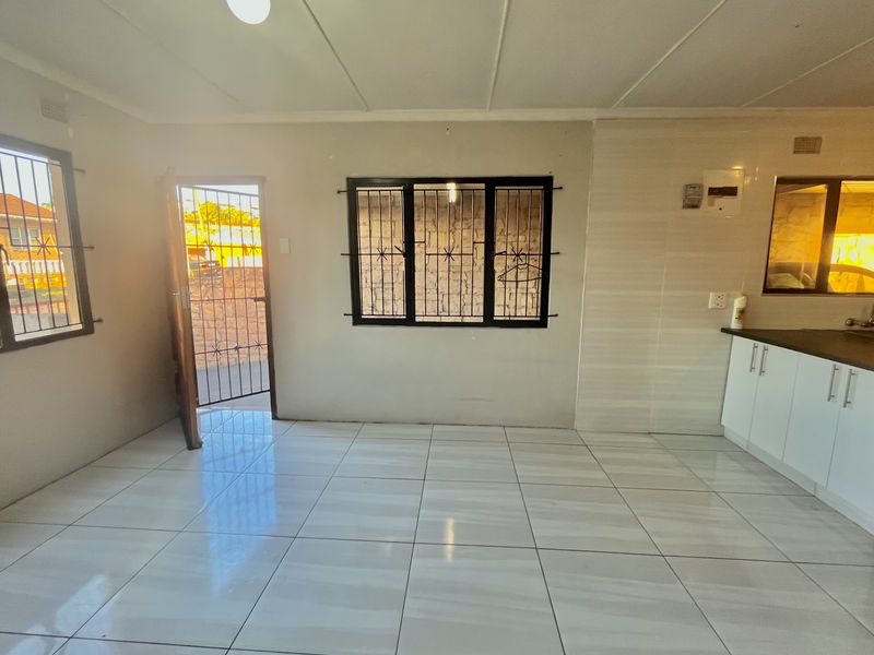 Open plan living and kitchen area featuring tiled flooring, security bars on windows, and basic kitchen cabinetry.