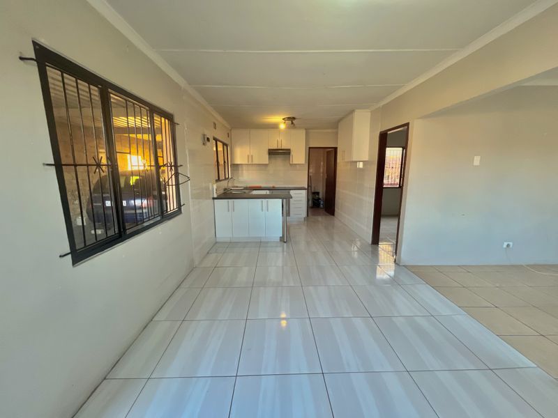 An open-plan living and kitchen area featuring tiled flooring, built-in cabinetry, and security bars on the windows, offering a clean, functional space.