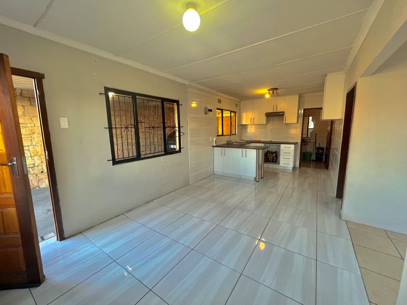 Open plan living and kitchen area featuring tiled flooring, built-in cabinetry, and security bars on windows.