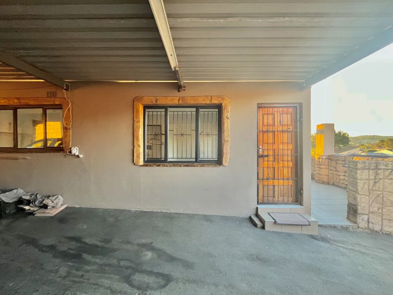 Covered entrance area featuring a security gate, stone-trimmed window, and corrugated metal roofing, providing a functional and secure access point to the property.