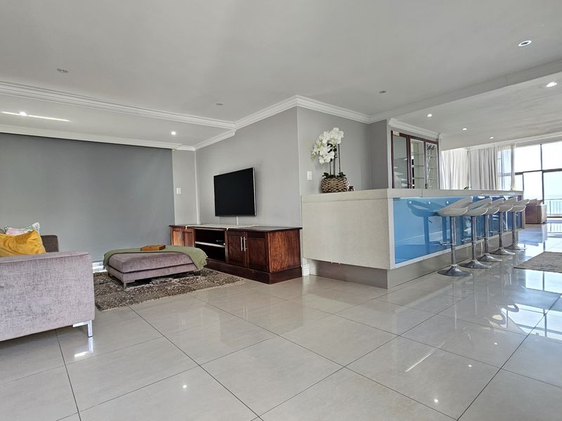 Spacious open-plan living area featuring polished tile floors, recessed lighting, a built-in bar counter, and a modern spiral staircase leading to upper levels.