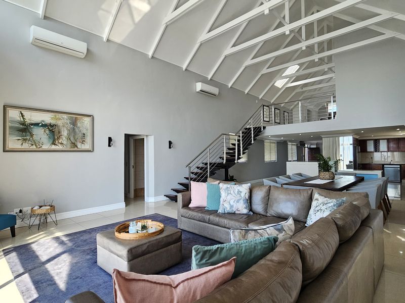 Spacious open-plan living area featuring a dramatic vaulted ceiling with exposed trusses, a mezzanine level, and a modern staircase with stainless steel balustrades.