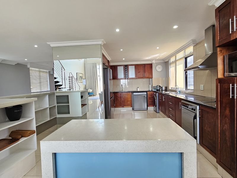 Spacious open-plan kitchen featuring dark wood cabinetry, stone countertops, a central island, and integrated appliances, seamlessly flowing into the living area.