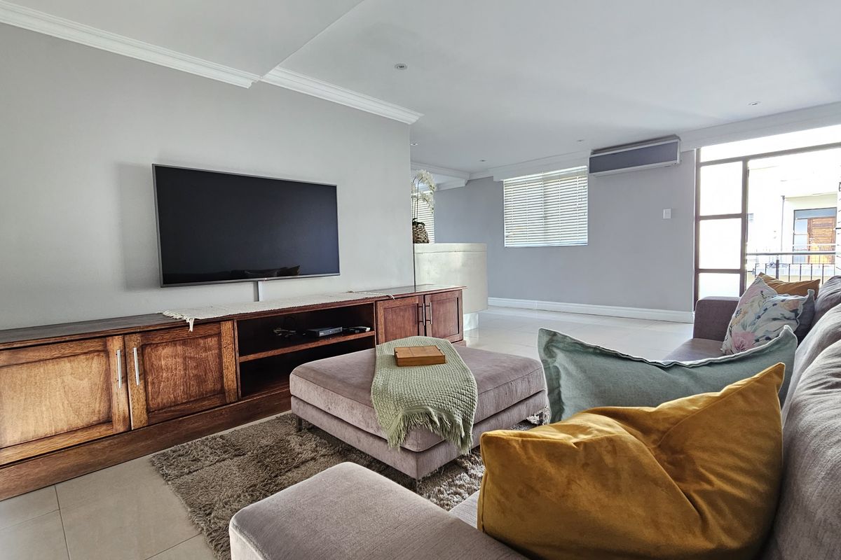A bright and spacious living room featuring neutral walls, crown molding, tiled flooring, and a wall-mounted air conditioning unit.