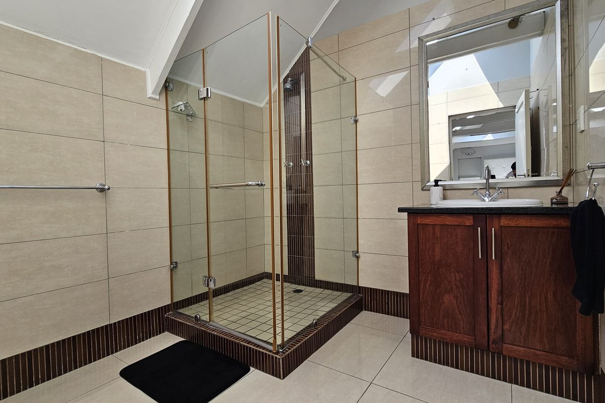 A well-maintained bathroom featuring a glass-enclosed shower, a wooden vanity with a basin, and neutral-toned wall and floor tiling under a pitched ceiling.