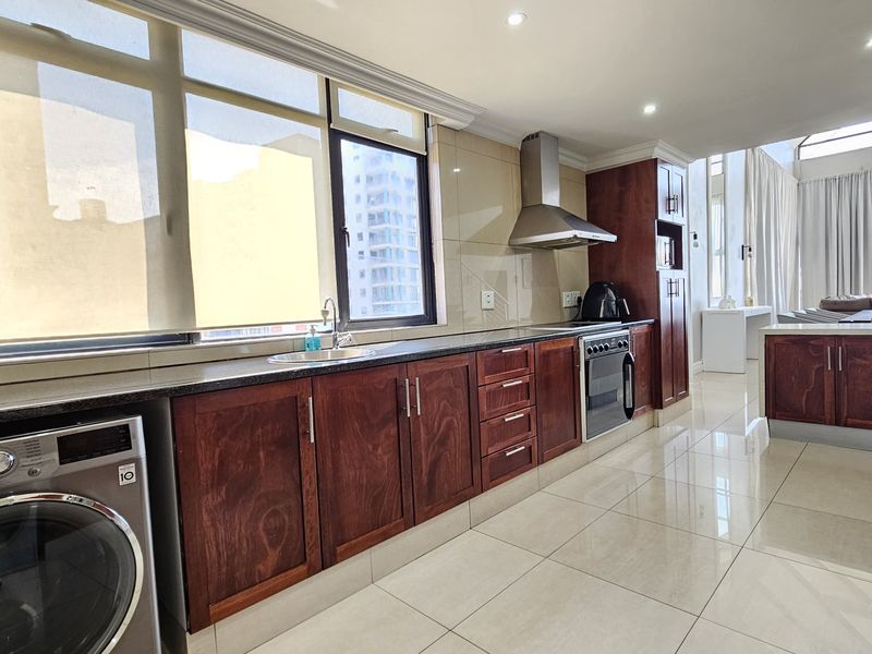Modern kitchen featuring dark wood cabinetry, granite countertops, stainless steel appliances, and large windows providing ample natural light in an open-plan layout.