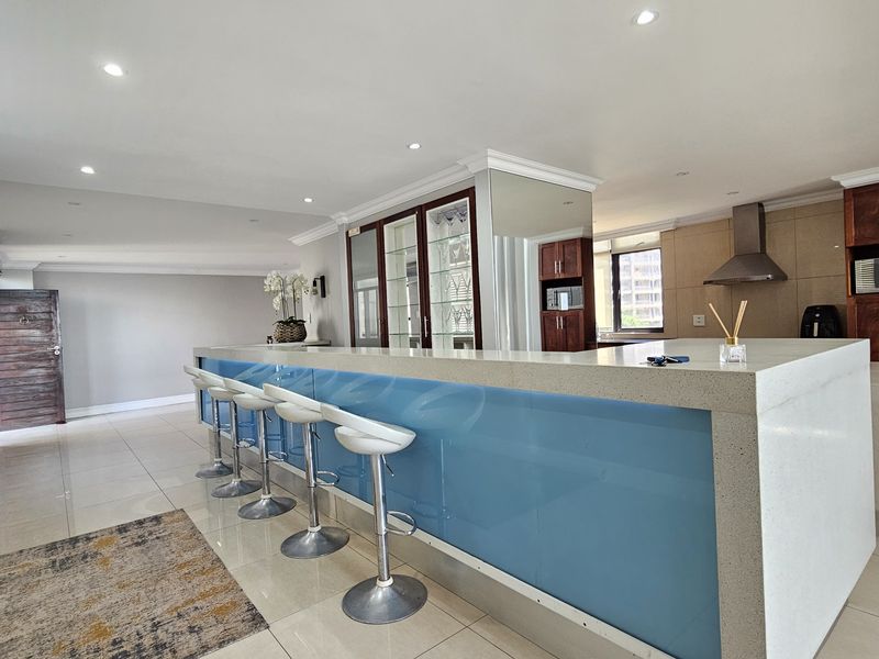 Spacious open-plan kitchen and living area featuring a large stone island, modern cabinetry, and recessed lighting in a contemporary penthouse setting.