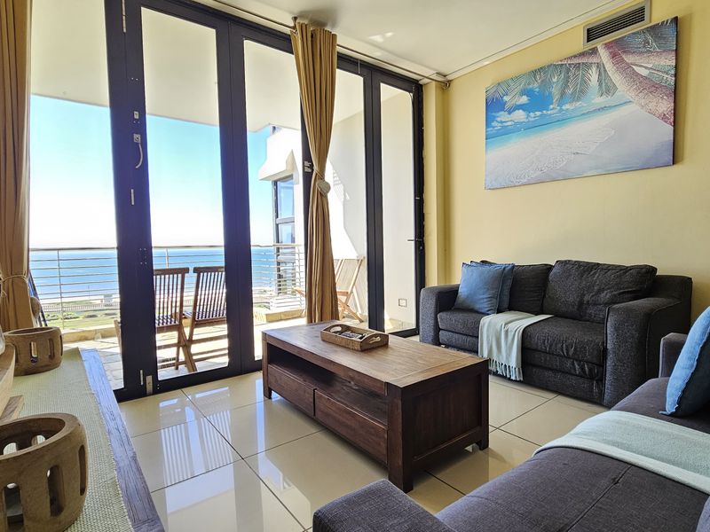 Bright living room featuring large glass sliding doors that open onto a balcony with ocean views and polished tiled flooring.